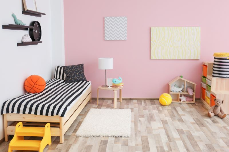 Quarto infantil com riqueza de diferentes texturas, com a cama feita em madeira de pinus, tapete felpudo, piso vinílico e papel de parede, mas respeitando a paleta de cores rosa e listrada de preto e branco.